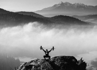 Este fanático del fitness levanta pesas en la cima de una montaña Este fanático del fitness levanta pesas en la cima de una montaña